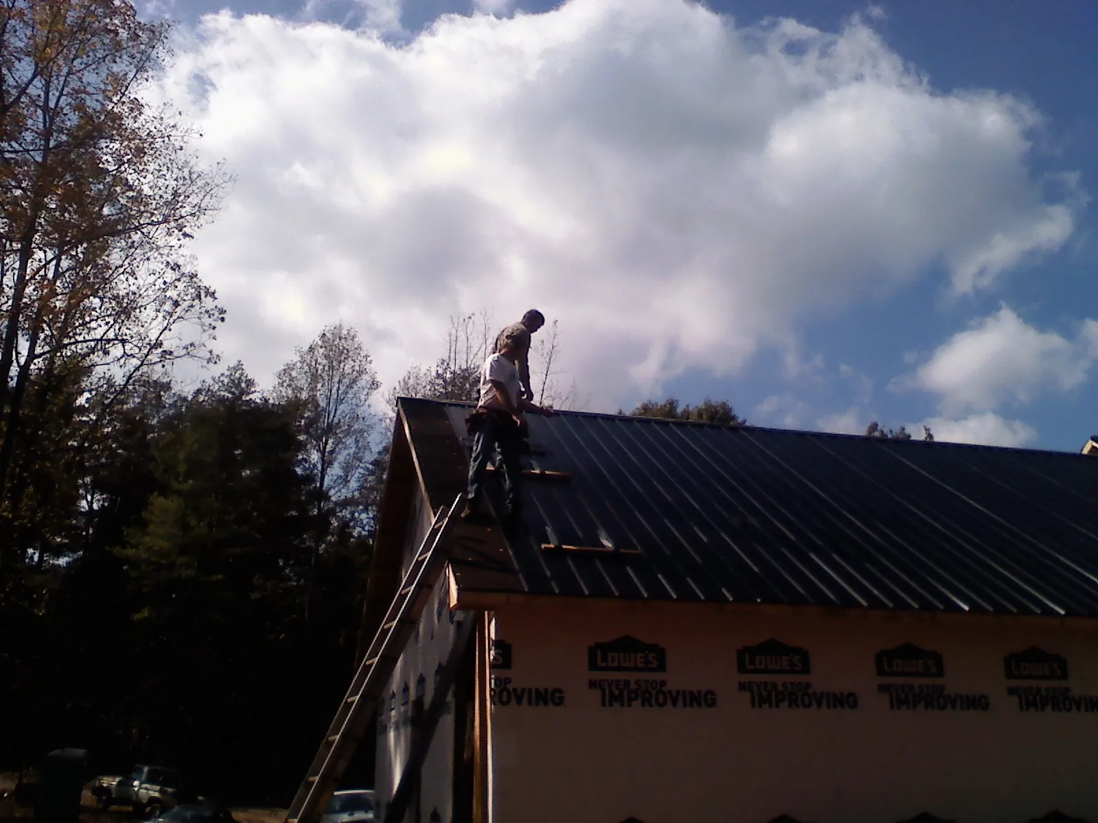 Roofer fastening dark metal panels high against a cloudy sky, from a Roof Inspection job in Williams